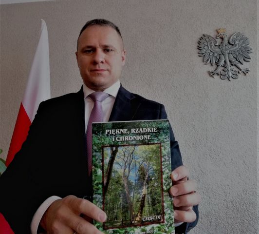 starosta Artur Berus trzyma w ręce nowo wydaną publikację pt. "Piękne, rzadkie i chronione" 