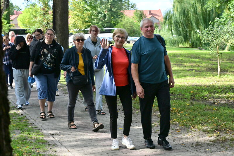 grupa turystów idąca aleją w parku. uśmiechnięta kobieta macha do obiektywu