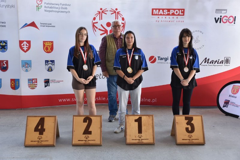 3 nastolatki z medalami na szyi na podium, z trenerem
